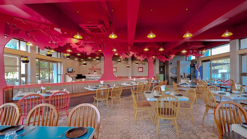 An image of a restaurant featuring chairs, tables, colourful tree cutouts on top with ceiling lights at Pride Resort Ambaji